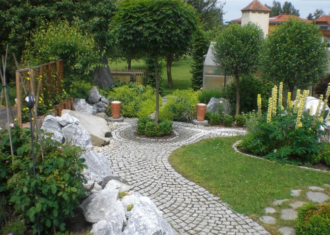 Ein gepflasterter Weg führt durch den Garten. Daneben liegen große Steine als Abgrenzung zum Beet.