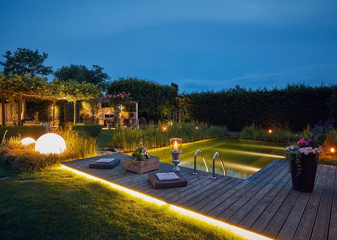 Indirekte Beleuchtung des Naturpools, des Holzstegs und der Pergola sowie Leuchtkugeln im Garten.