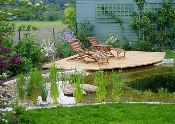 Kleiner Schwimmteich mit kleinem Holzsteg. Darauf stehen zwei Liegen aus Holz.