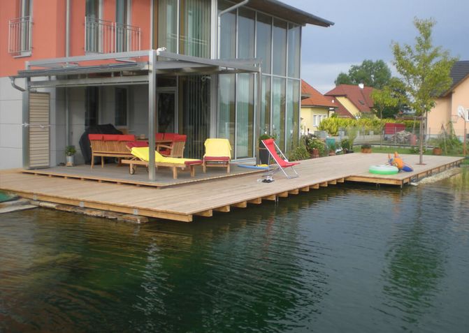 Haus, dessen Terrasse mit einem großen Holzsteg vom Schwimmteich getrennt ist.