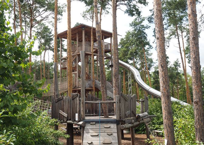 Der Rutschenturm im Abenteuergarten, inmitten von schattenspendenden Bäumen.