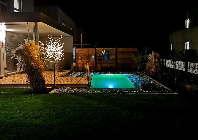 Ein Garten bei Dunkelheit. Der NANO Teich und die Terrasse haben eine Beleuchtung.